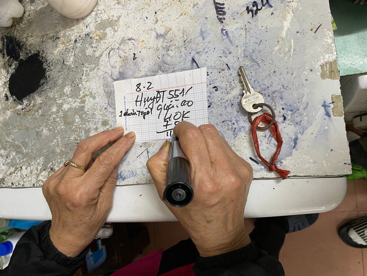 Sau khi nhận đồ của khách, bác Nhung cẩn thận ghi tên thông tin hàng hóa và thông tin người giặt để phân loại.