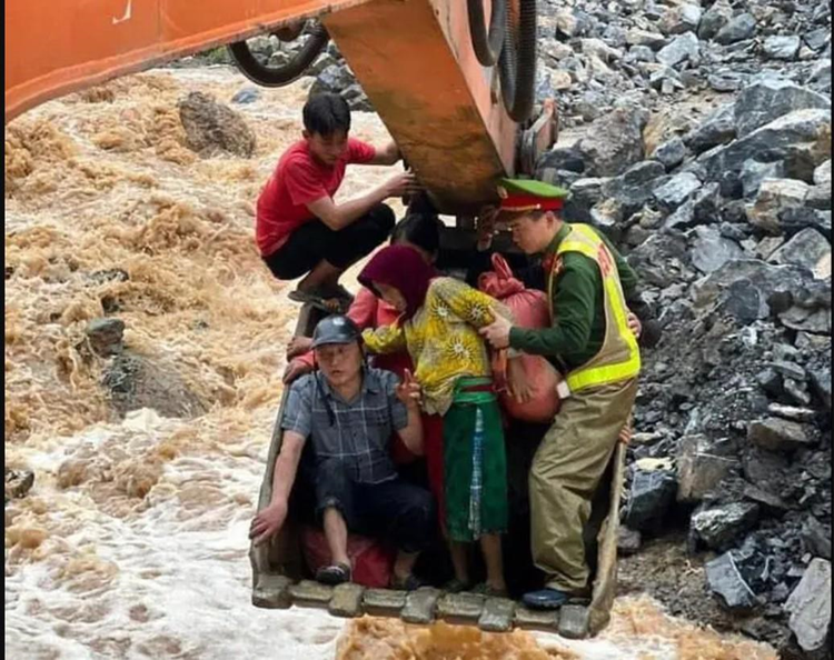 Thượng úy Tường và người dân phải ngồi trong gầu máy xúc để thoát khỏi khu vực nguy hiểm. Ảnh: Công an Nhân dân. Thượng úy Tường và người dân phải ngồi trong gầu máy xúc để thoát khỏi khu vực nguy hiểm. Ảnh: Công an Nhân dân.