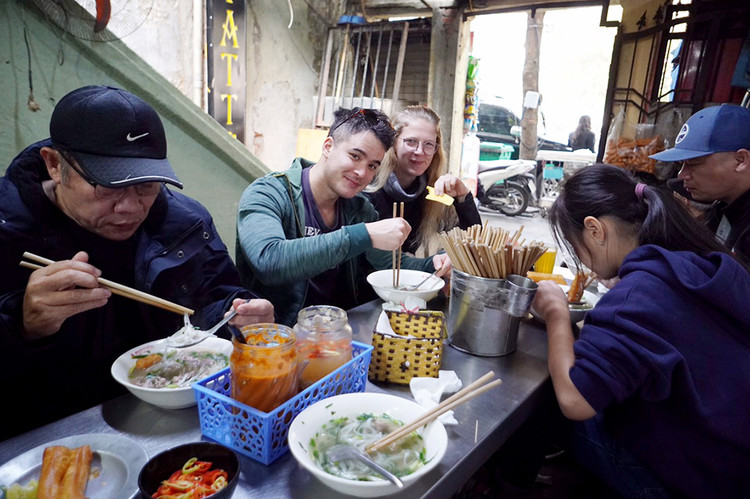 Hai du khách nước ngoài thích thú được trải nghiệm món phở đặc trưng của Hà Nội.