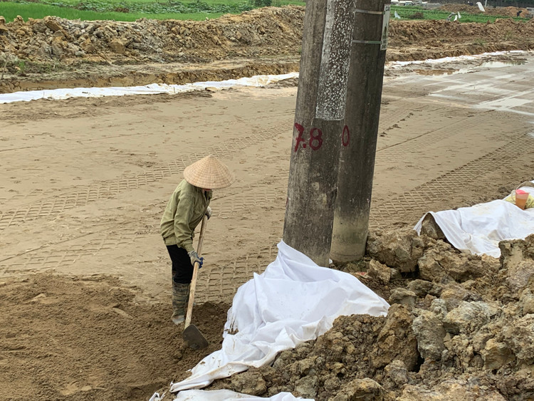 Một công nhân đang san gạt cát ngay bên chân cột điện.