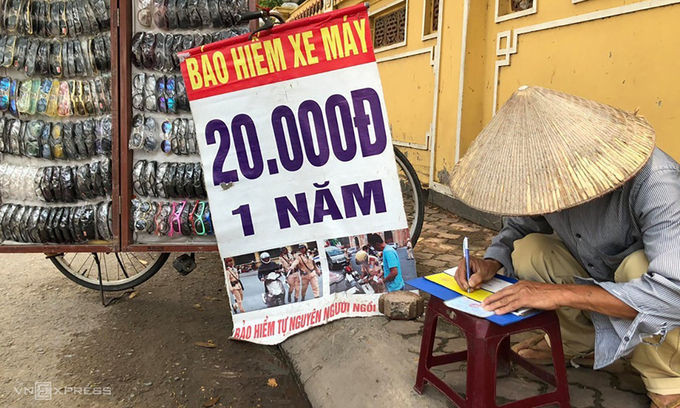 Một bán kính măt, kiêm bán bảo hiểm xe máy viết giấy chứng nhận cho khách tại lề đường Hồ Tùng Mậu trưa 18/5. Ảnh: Anh Tú