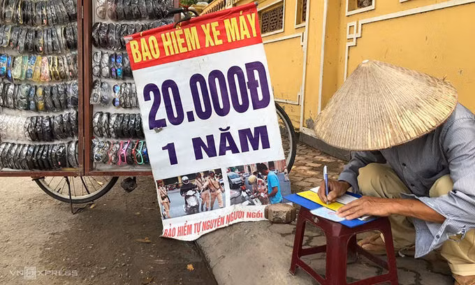 Một bán kính măt, kiêm bán bảo hiểm xe máy viết giấy chứng nhận cho khách tại lề đường Hồ Tùng Mậu trưa 18/5. Ảnh: Anh Tú