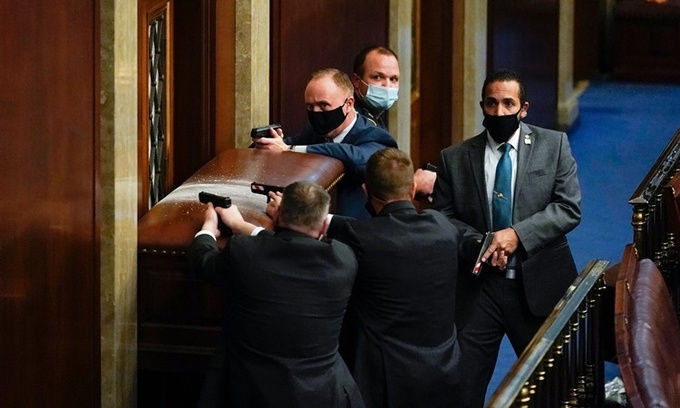 Nhân viên an ninh chĩa súng về một trong những cánh cửa của phòng họp Hạ viện Mỹ để cảnh giới khi những người biểu tình gây náo loạn ở bên ngoài. Ảnh: AP. 