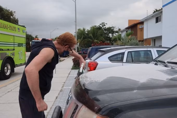 Một người đàn ông sống gần chung cư sập phủi bụi trên ô tô sáng 24/6. Ảnh: WLRN.