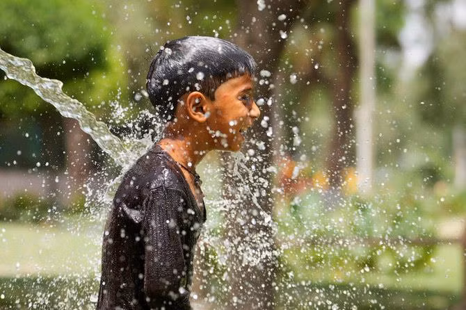 Một cậu bé làm mát mình dưới đường ống nước tưới tiêu ở bang Uttar Pradesh miền bắc Ấn Độ hôm 19/44. Ảnh: AP