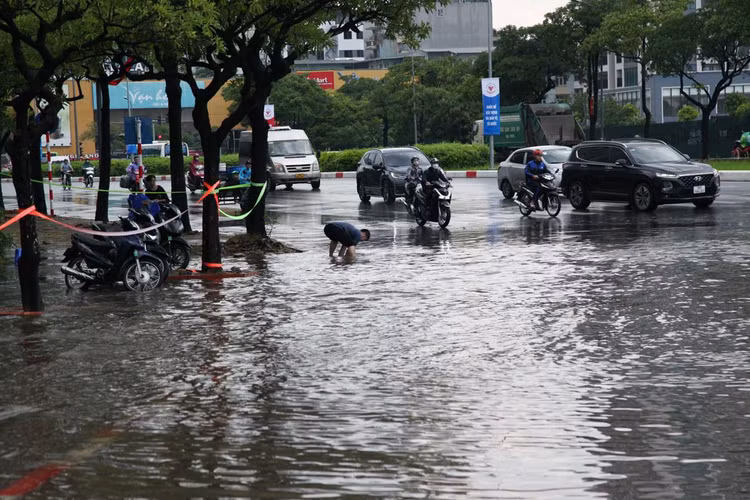 Người dân lội nước gỡ rác ở nắp cống thoát nước.